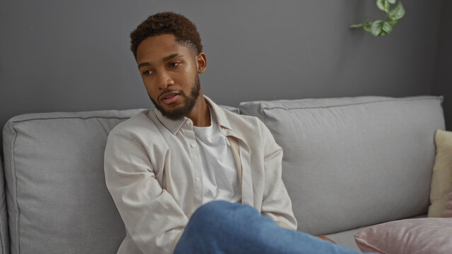 Young man sitting on a couch in a modern living room, looking thoughtful and relaxed, with a stylish interior setting and neutral color tones