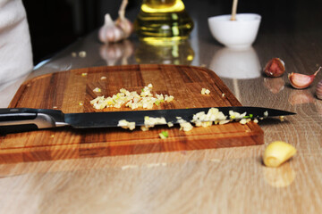 minced garlic on a board. Knife and garlic on the kitchen board. Oil, garlic, pepper, pungent, strong unpleasant odors in the kitchen