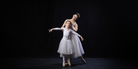 Adult ballerina guiding child in ballet posture, gently supporting arms, both dressed in white...