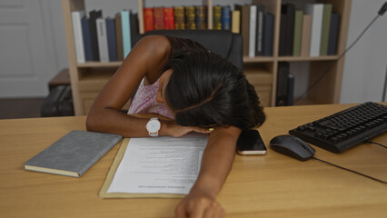 Young woman sleeping on office desk with documents, phone, and mouse nearby in an indoor workplace