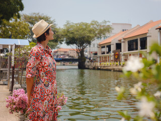 Fototapeta premium Young woman in ethnic dress and hat exploring the vibrant streets of Malacca, Malaysia. A blend of cultural heritage, colorful architecture, and tropical charm. Perfect travel and lifestyle moments.