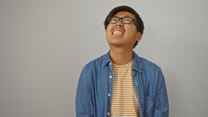 Fototapeta premium Young man, chinese, looking frustrated upwards, isolated against white background, wearing glasses and denim jacket, conveying emotions of anger and annoyance.
