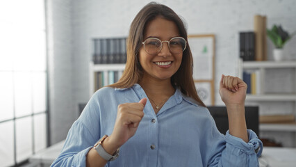 Young woman celebrating success with a smile in a modern office, showcasing a positive and...