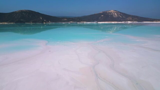 A turquoise tailings pond near a cement factory, surrounded by rugged hills. The vivid water contrasts with the barren land, creating a striking yet industrial scene of environmental impact