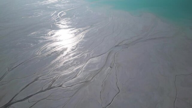 A turquoise tailings pond near a cement factory, surrounded by rugged hills. The vivid water contrasts with the barren land, creating a striking yet industrial scene of environmental impact