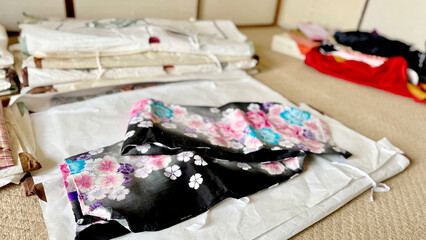 たとう紙の上に置かれた黒地に花模様の浴衣と複数の着物