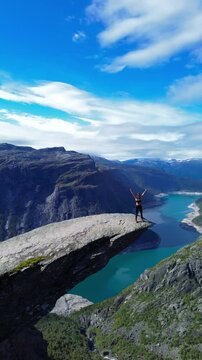 A woman hiker walking on the iconic Trolltunga rock in Norway, surrounded by breathtaking natural beauty. A perfect outdoor adventure in Norway&rsquo;s majestic mountains, ideal for hiking and nature lovers