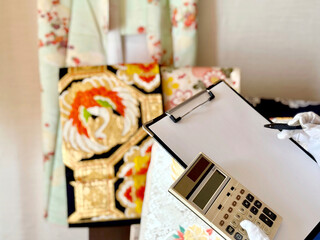 クリップボードと計算機を持って着物と帯を査定する人