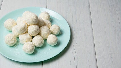 Blue plate with delicious homemade candies with coconut flakes and almonds stands on a light wooden table, background with copy space