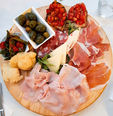 Italian appetizers including bruschetta, olives, vegetables, cheese, ham and salami resting on wooden cutting board