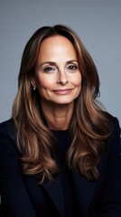 Fototapeta premium Studio portrait of a stylish middle-aged woman with long hair, smiling softly against a neutral background.