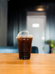 A transparent plastic cup americano coffee on wood table