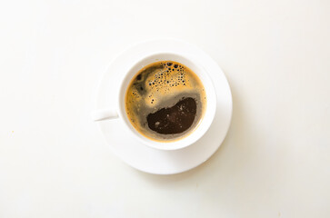 White cup and black coffee on white table in top view