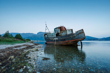 shipwrecked boat on shoreline with mountains in background