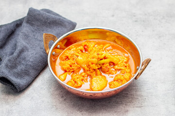 a bowl of vibrant yellow curry featuring cauliflower and potatoes, served in a traditional Indian-style copper dish.