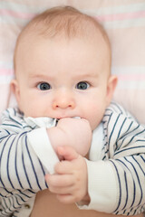 child beautiful happy boy with black eyes holds hands in mouth, close-up