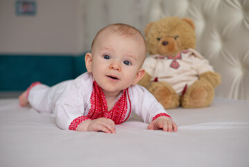 beautiful child boy lying on bed in Ukrainian embroidered shirt with teddy bear toy