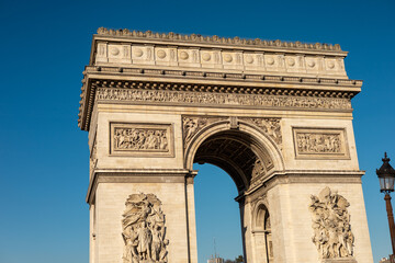 Fototapeta premium Visitors admire the impressive architecture of the Arc de Triomphe under clear blue skies in Paris