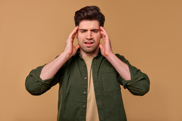 A Stressed Young Man is Holding His Head with Frustration Against a Brown Background