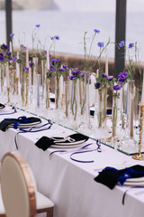 Wedding table decor with purple flowers in glass vases, gold candleholders, and pearl accents on a...