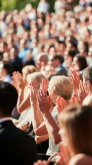 A diverse audience is seated in an outdoor amphitheater, applauding. The image captures a lively, sunlit gathering with a focus on hands clapping.