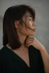 Fototapeta premium A close-up portrait of an Asian girl with freckles, plump lips, and a beauty mark above her upper lip, standing in the sand dunes during the golden hour. The warm sunset light accentuates her natural 