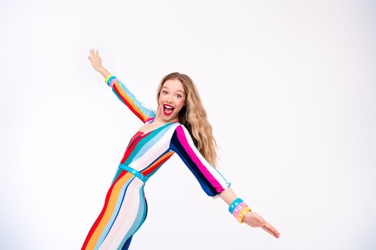 Young woman in colorful striped overall poses joyfully against a white background, capturing a vibrant and youthful style