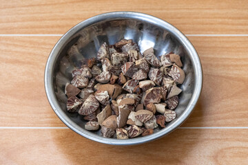 Betel nut fruit (Areca catechu), locally known as Supari in Bangladesh, is cut into small pieces on a steel plate against a wooden background. Betel nuts are used in paan masala.