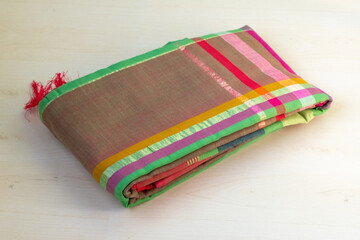A folded green cotton saree rests on a wooden backdrop. Sarees are a common attire for Bangladeshi women, worn at weddings, festivals, and even daily.