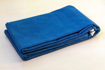 A folded blue cotton saree rests on a light wooden backdrop. Most Bangladeshi women wear sarees to weddings, festivals, and also on a daily basis.