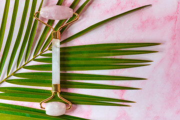 Pink Gua Sha stone roller on palm leaf and marble background. Top view. Flat lay.
