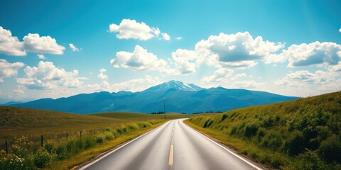 Asphalt road leading to a snow-capped mountain peak under a vibrant blue sky with fluffy white clouds and lush green hillsides