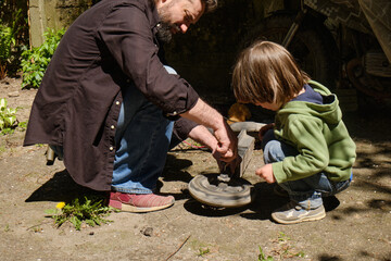 Father and young son working together repairing a bicycle wheel in a backyard setting. Bonding moment with focus on teamwork and learning practical skills outdoors. 