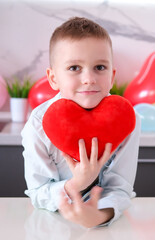 Charming, joyful, smiling boy with heart-shaped toy in his hands for Valentine's Day. Concept of celebration and love. Greeting card. Vertical photography.