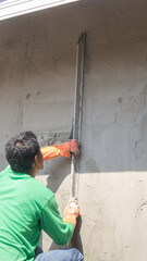 A male plastering worker sweeps away excess cement from his work area in an outdoor construction site.
