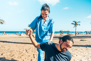 A doctor in a blue scrubs is helping a man with his arm at the beach