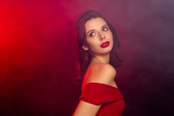 Portrait of a glamourous young woman in red dress, accented by dark background and warm red...