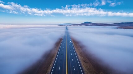 Fototapeta premium Road Through the Clouds - A scenic aerial view of a highway cutting through a low-lying cloud layer, a single vehicle visible on the road.
