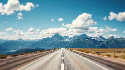Naklejka premium Asphalt Road Stretching Towards Majestic Mountain Range Under a Blue Sky with Fluffy White Clouds