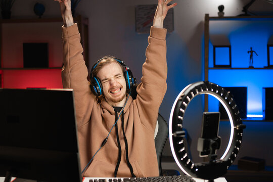 blogger young gamer broadcasts live streaming to review video game on social media, celebrating winner victory triumph, reviews for video blog. Influencer uses smartphone and ring lamp.