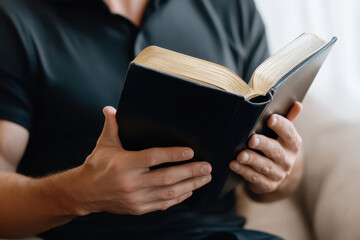 Obraz premium Man holds open black Bible looking down, showcasing faith and reflection with gentle hands