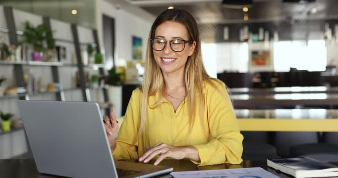 Woman working on project, sit at table with laptop and papers, reviewing and analyzing documents or reports involving graphs or charts, make calculations, preparing presentation, or summarizing data