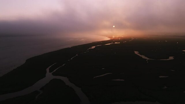 Aerial dawn view over the River Taw estuary with dark shore, towards the rising sun obscured in mist