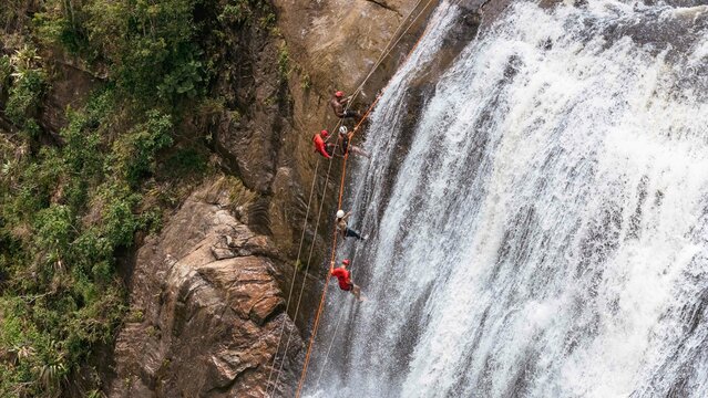 Aerial shot of a group of people abseiling a high waterfall