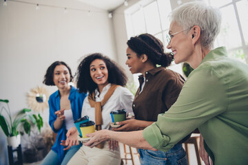 Photo of four diverse women businessladies feminists cafe drink share coffee paper cup takeout office loft room interior indoors workspace