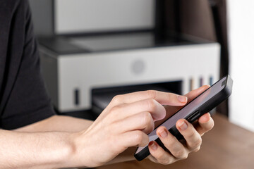 Using a Smartphone to Control a Wireless Printer, Hands Navigating the Screen with a Printer Visible in the Background