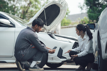 Assessing the Damage:  A mechanic and a customer inspect the front end of a car following a fender...