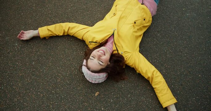 A happy girl in a yellow jacket lies on the asphalt and rejoices after the rain in the city in summer