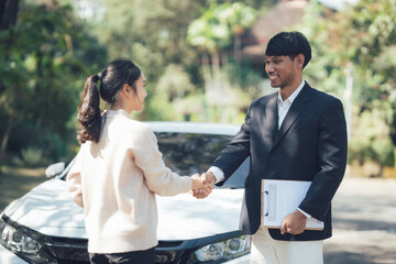 Successful Deal: A man and woman shake hands in front of a car, signifying a successful deal. The...