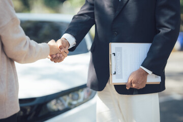 Successful Car Deal: A handshake seals the deal between a car salesperson and a customer,...